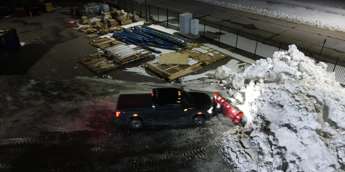 Snow removal vehicle clearing snow from a commercial parking area at night