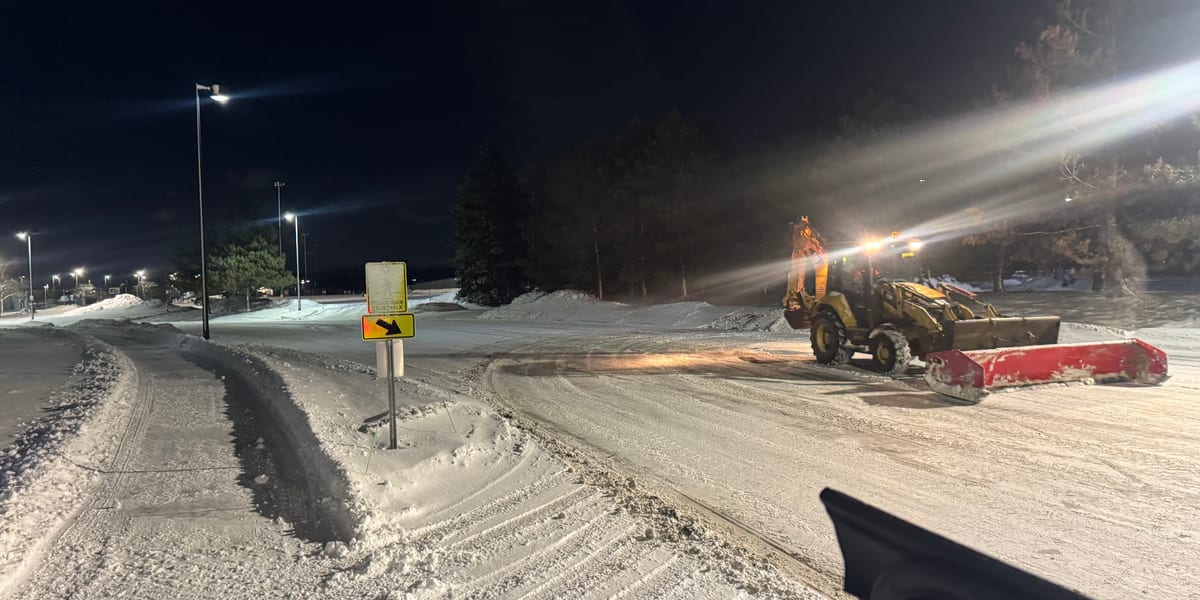 Snow plow truck spreading deicing material on a snow-covered road at night
